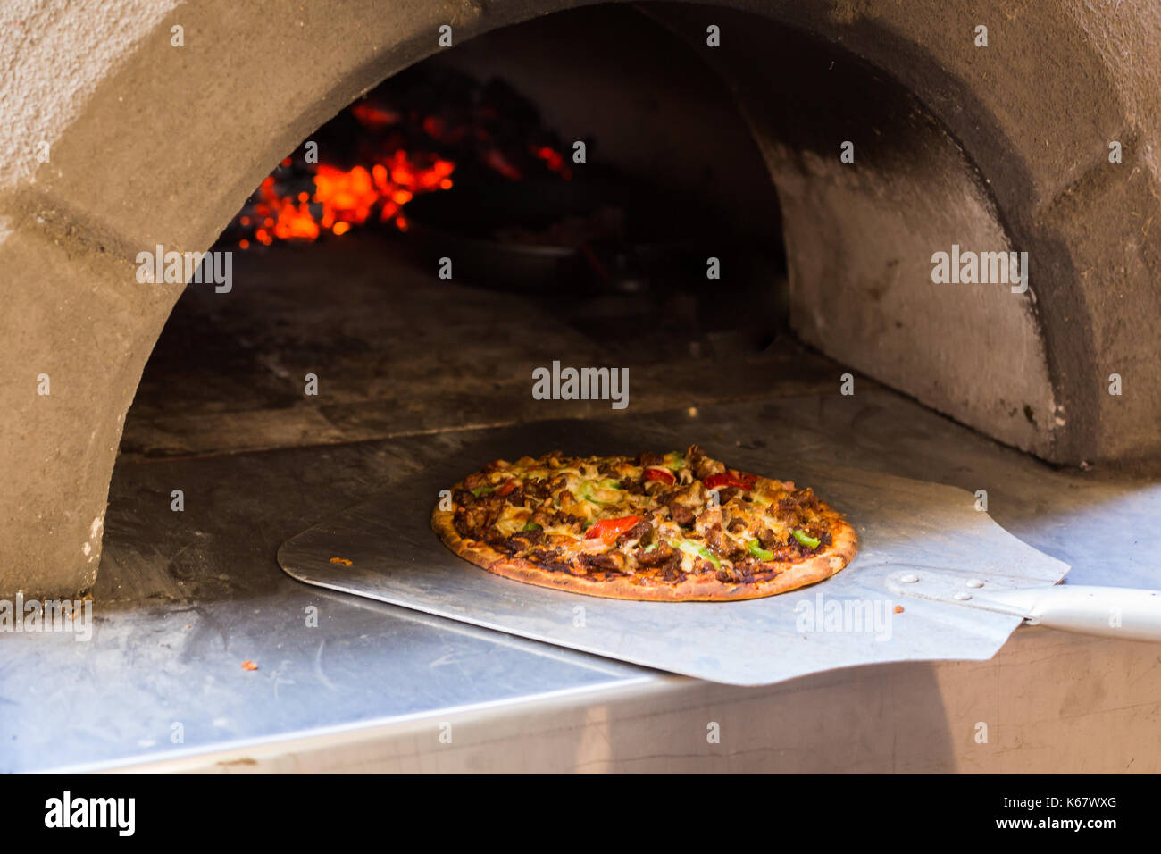 Removing a pizza from wood-fired pizza oven Stock Photo