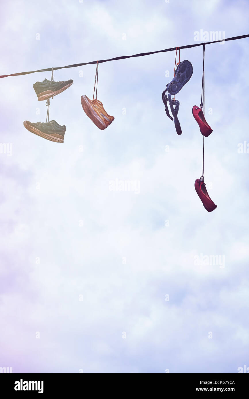 Vintage stylized picture of old dirty shoes hanging on wire, space for text. Stock Photo