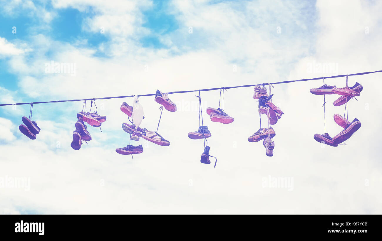 Vintage stylized picture of old dirty shoes hanging on wire. Stock Photo
