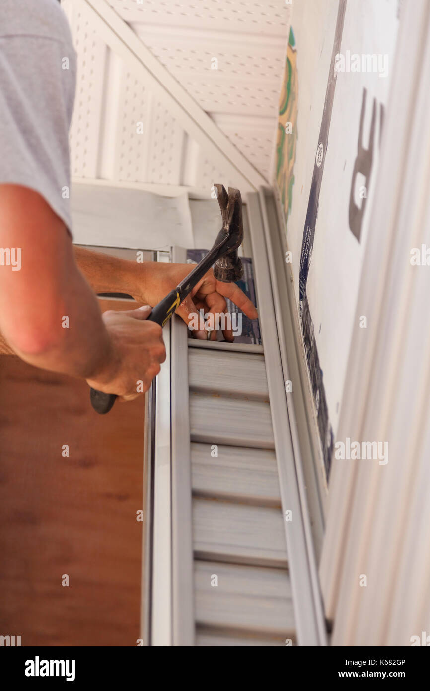 A construction worker hammering a nail to secure vinyl siding around