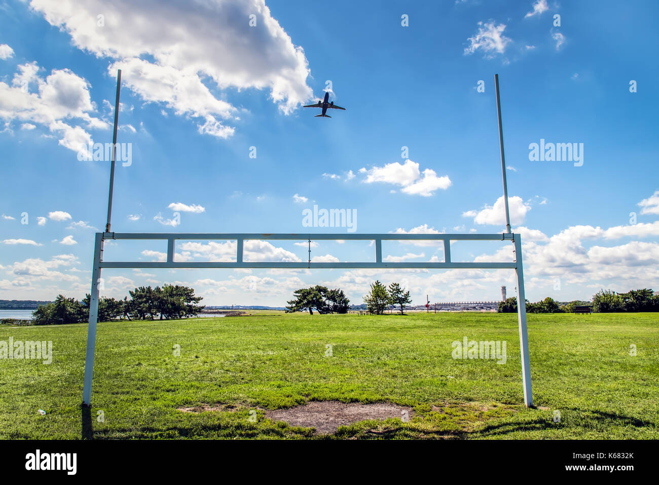 An airplane takes off over the football goal posts of a nearby ball park. Stock Photo