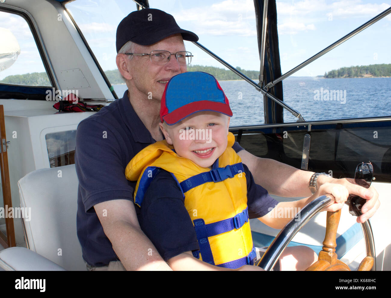 grandfather holding his small grandchild, teaching him to drive a boat Stock Photo