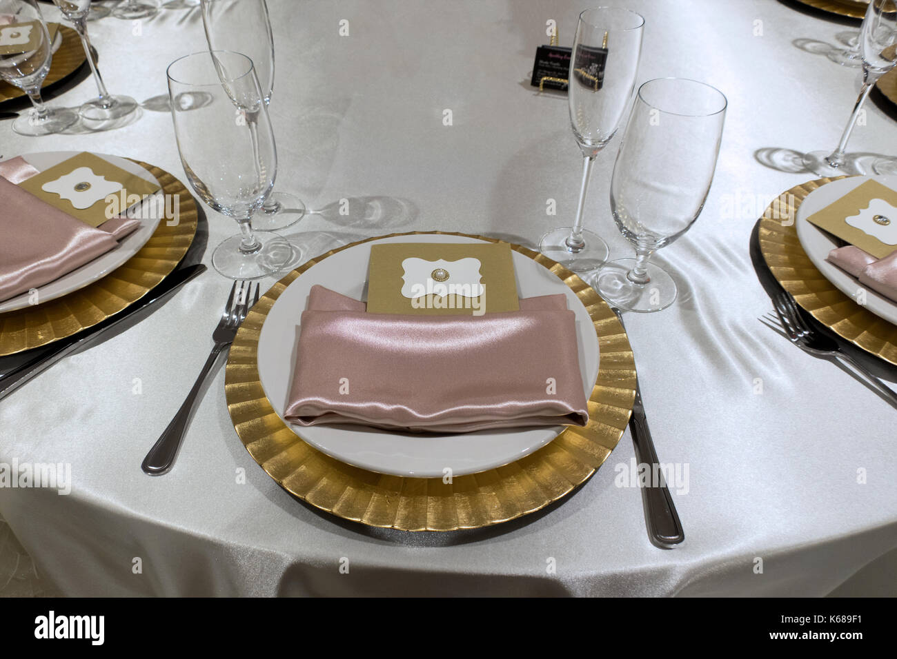 A fancy place setting with a golden plate, pink napkins, and an