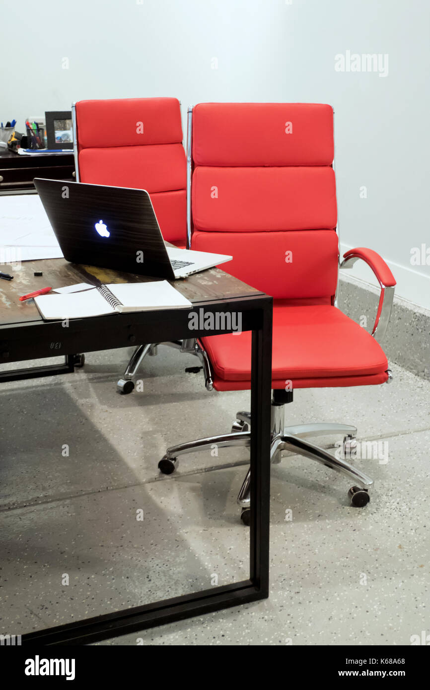 Two red office chairs sitting at a table with a mac book laptop sitting open beside a stack of papers. Stock Photo