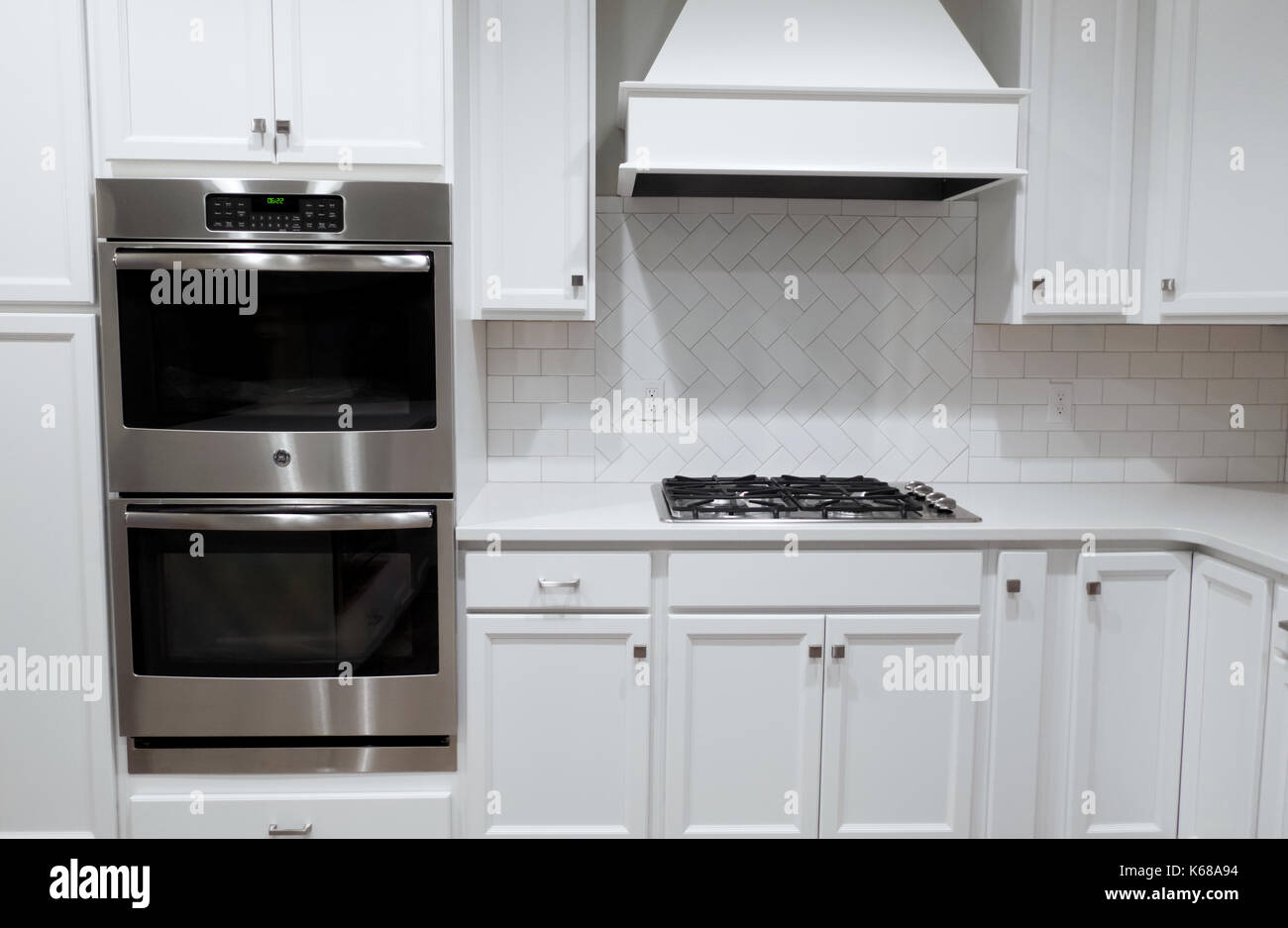 A white kitchen with stainless wall ovens, a gas stove and a range hood. Stock Photo