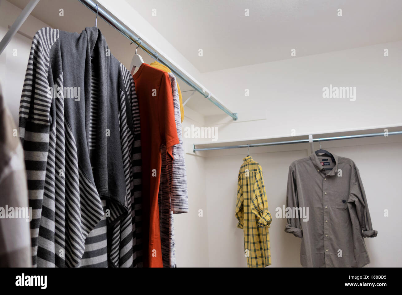 A walk in closet with men's short sleeve shirts and woman's sweaters and scarves. Stock Photo