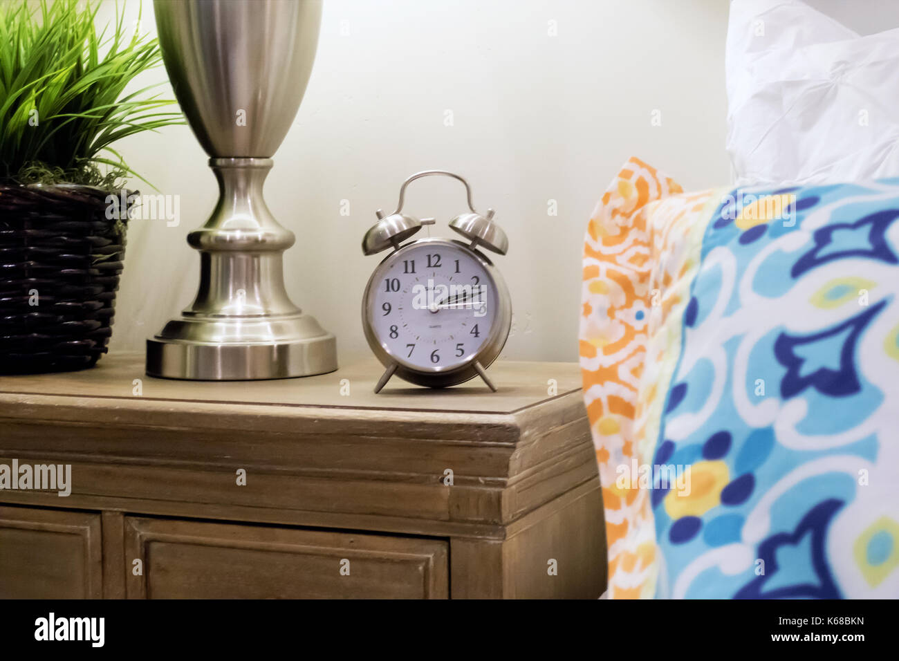 An old fashioned clock on a nightstand beside a bed Stock Photo Alamy