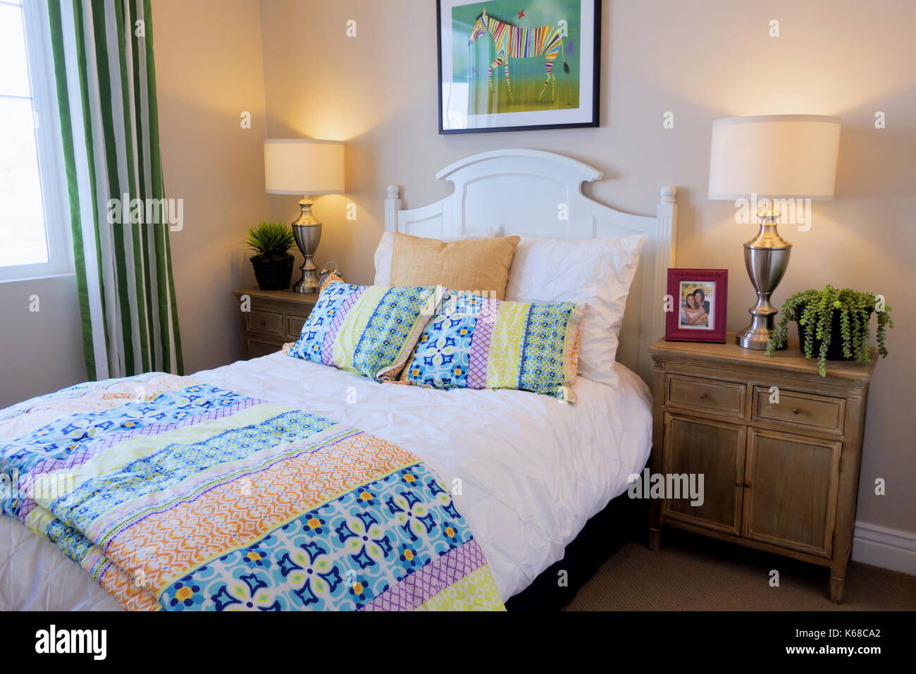 A light bedroom with two nightstands, a lamp and a colorful comforter in a cozy setting. Stock Photo