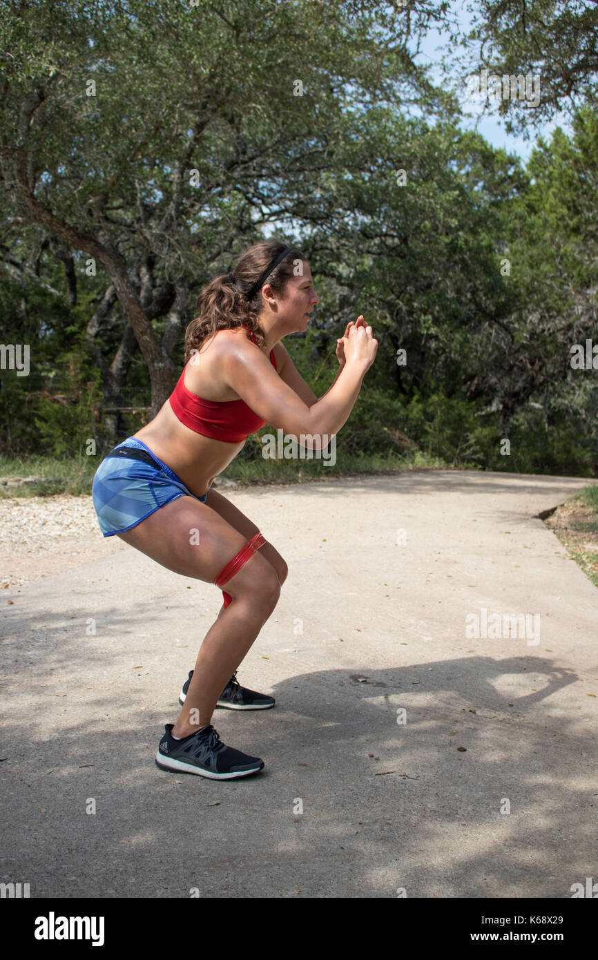 Young woman working out on her drive wearing red sports bra and shorts doing squats Stock Photo