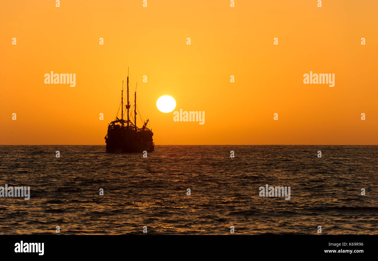 Ocean sunset ship silhouette is an old wooden ship sitting at sea watching the sunset on the ocean horizon. Stock Photo