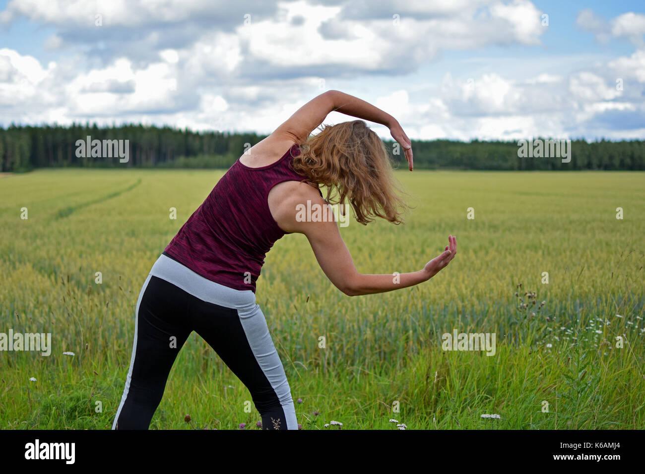Middle aged yoga woman stretching and exercise outdoors. Rear view, field on background. Stock Photo