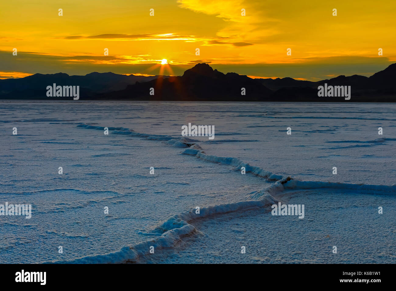 In this shot a'pressure ridge' of salt snakes out across the Bonneville Salt Flats as the sun sets over the Silver Island Mountains in the distance.   Stock Photo