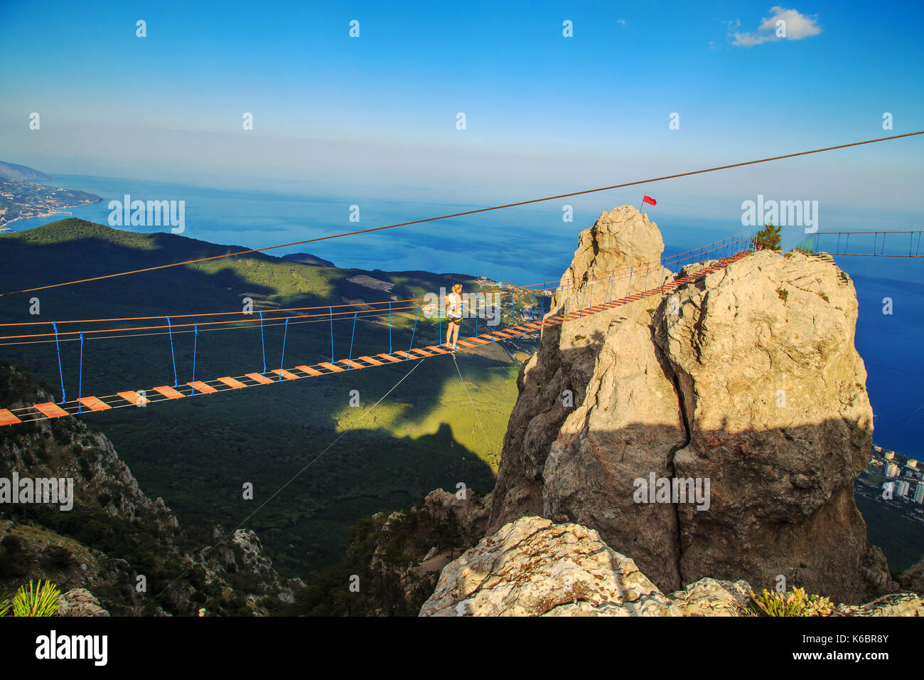 Woman is walking along a suspension bridge over an abyss. Yalta, the Crimea. The concept of risk and danger. Stock Photo
