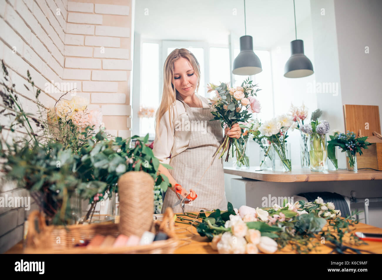 Florist workplace: woman arranging a bouquet with roses, matthiolas, ranunculus flowers and gypsophila paniculata twigs. Stock Photo