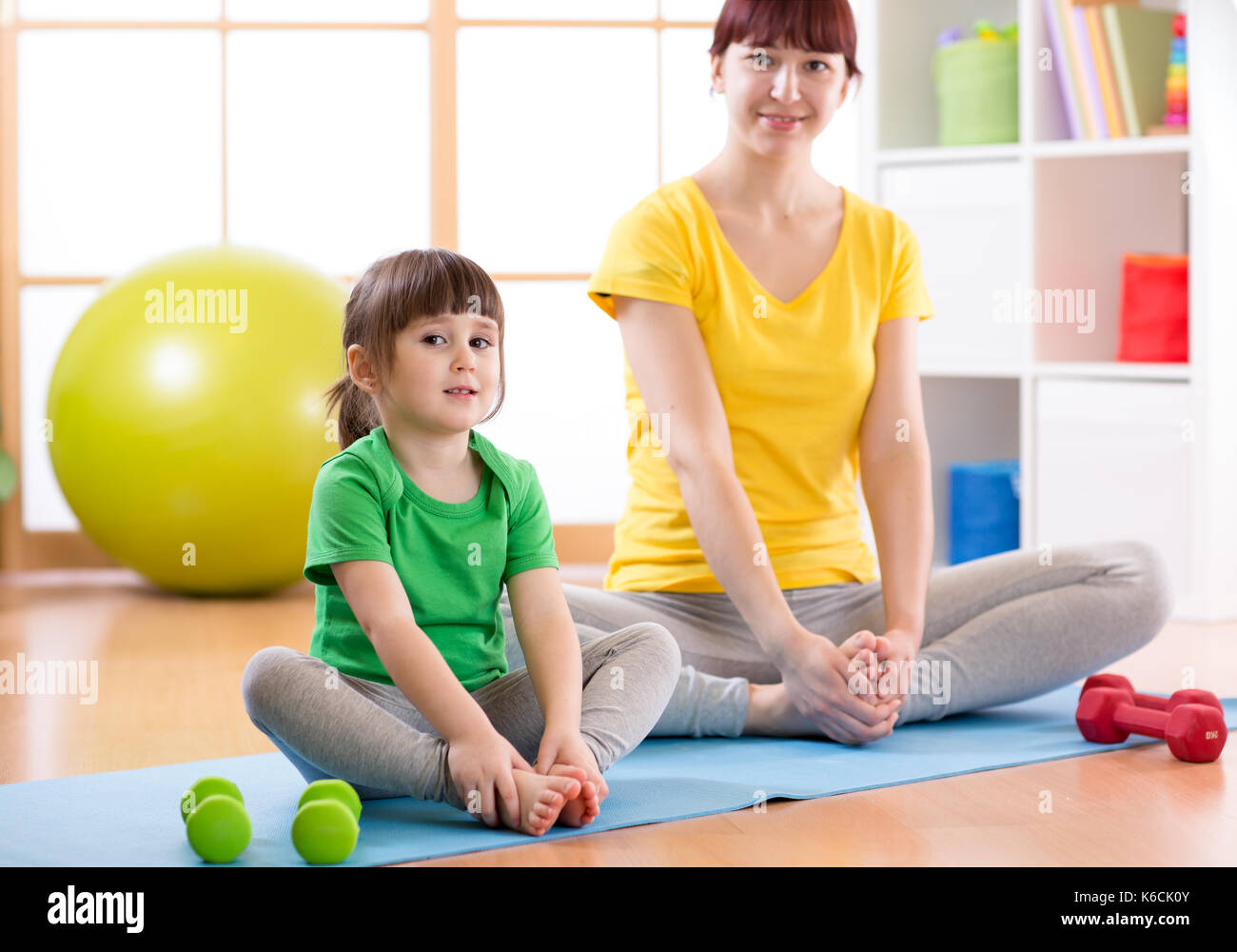 Mother and daughter doing fitness exercises on mat at home Stock Photo