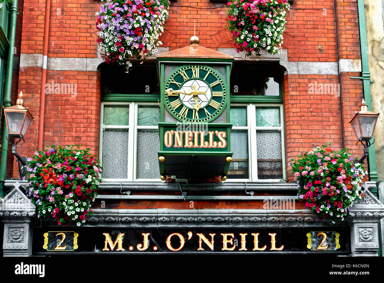 Large green clock, lamps, pub sign, flowers on the wall outside M.J. O'Neill's bar. Traditional Irish pub. Dublin. Republic of  Ireland, Europe, EU. Stock Photo
