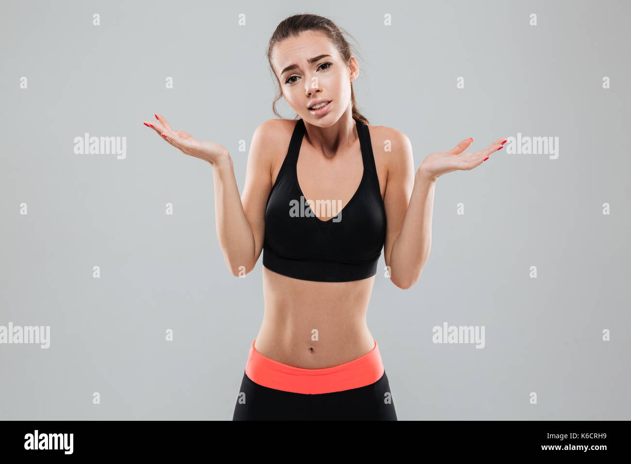 Sports woman shrugging shoulders and looking at the camera over gray background Stock Photo