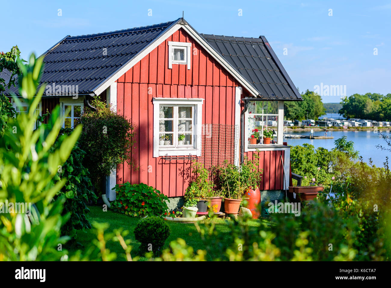 Karlskrona, Sweden - August 28, 2017: Travel documentary of city gardens. Red vintage coastal cabin with flowerpots in garden. Sea and camping area in Stock Photo