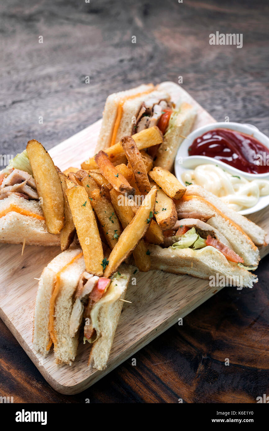 classic gourmet club sandwich with fries on wooden board Stock Photo