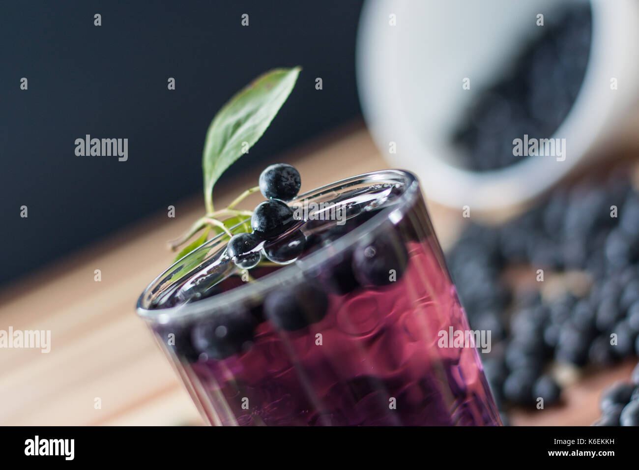 Bowl full of aronia spilled on wooden table with glass of aronia juice Stock Photo