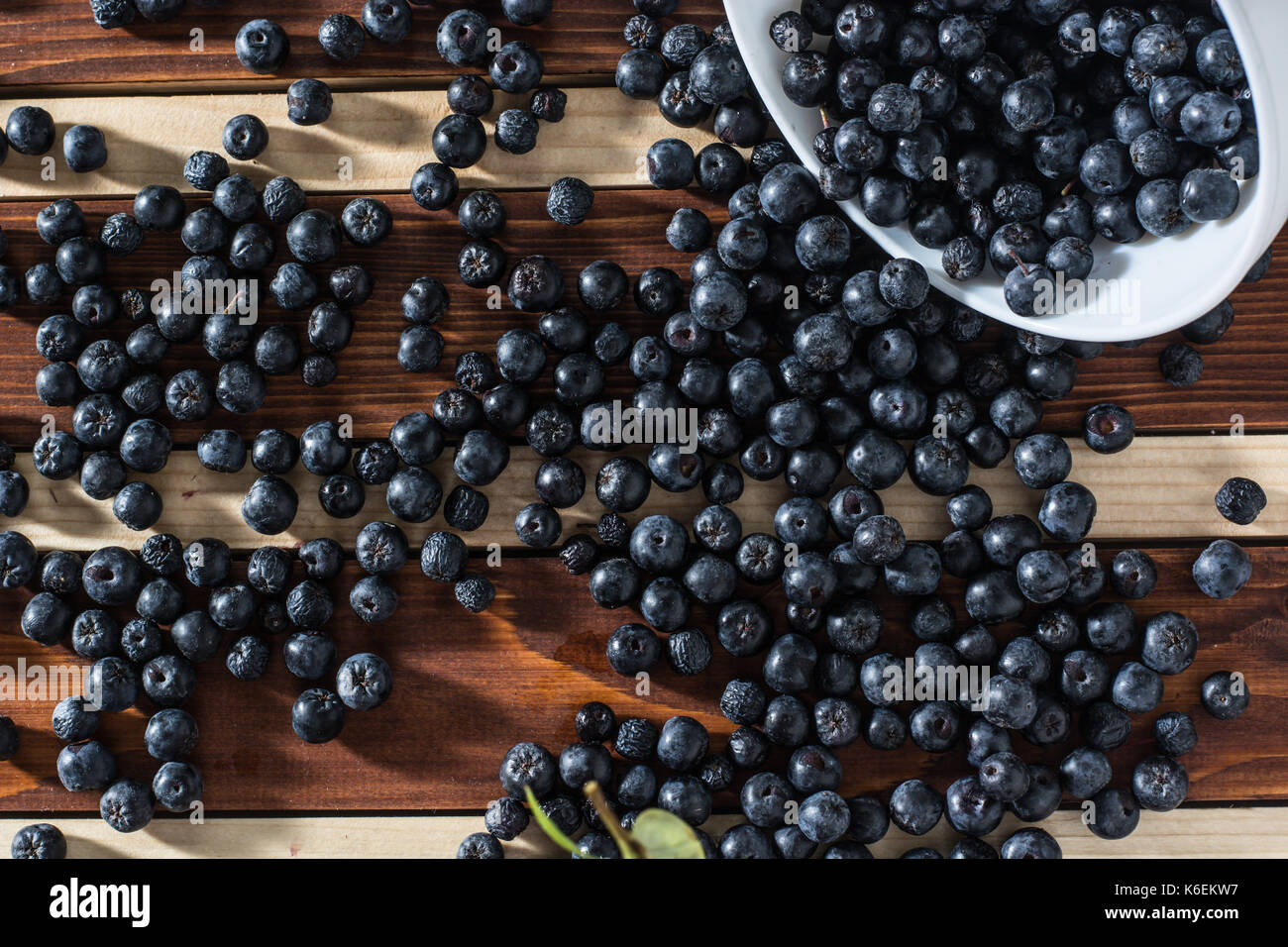 White bowl full with fresh and tasty aronia spilled on wooden table Stock Photo