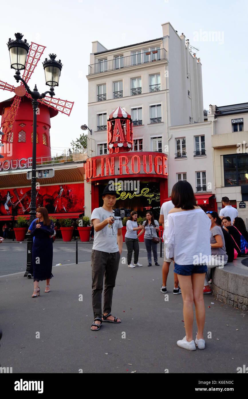 Chinese tourist takes a photo of himself in front of the Moulin Rouge in Paris, using a selfie stick Stock Photo