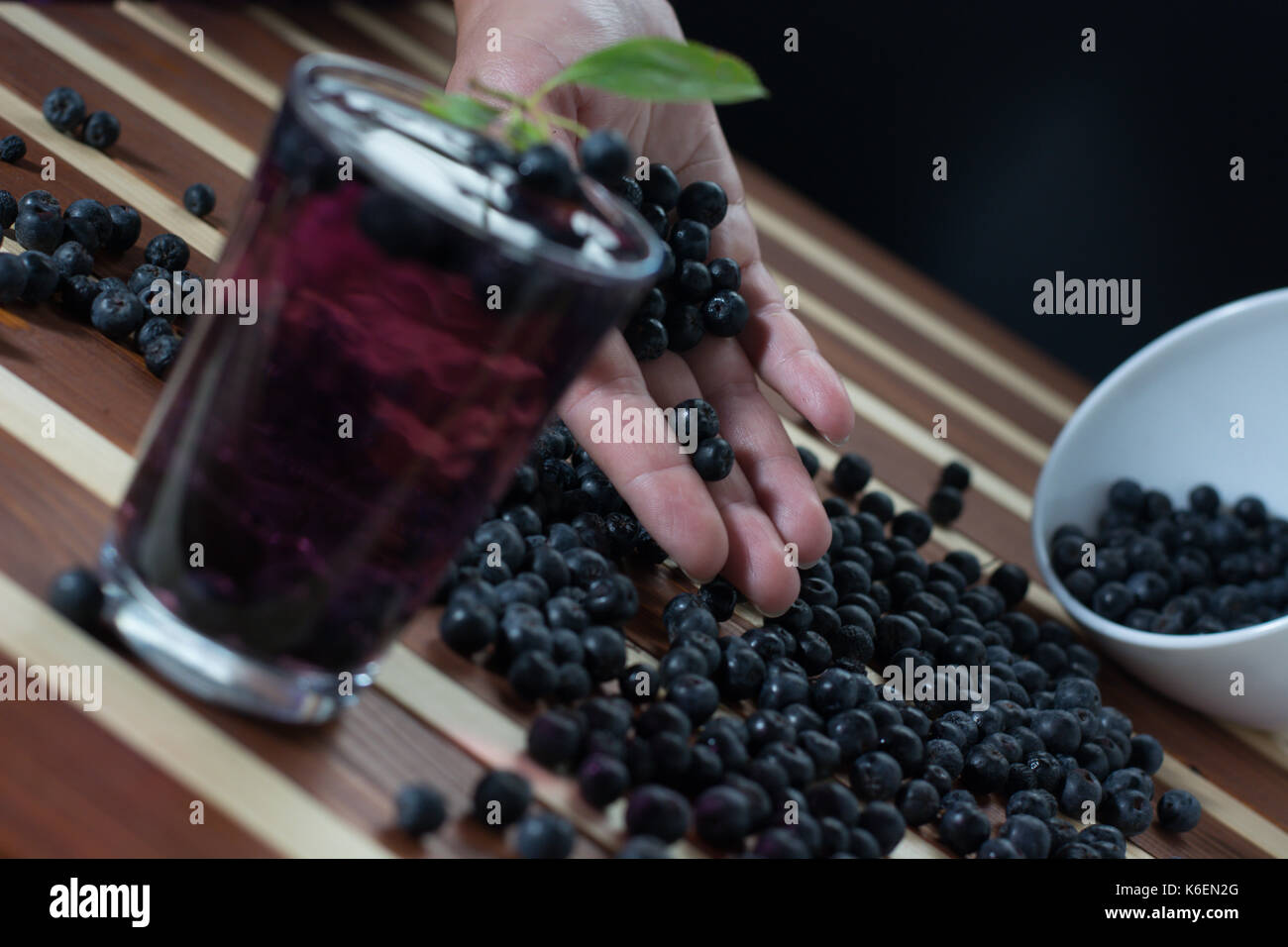 Female hand with aronia and bowl full of aronia spilled on wooden table with glass of aronia juice Stock Photo
