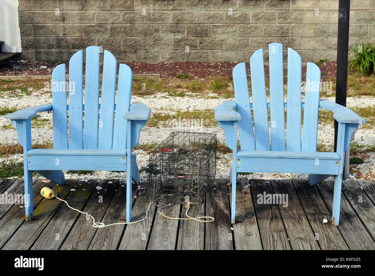 Two Light Blue Adirondack Chairs on a dock with a Crab Pot in between them Stock Photo