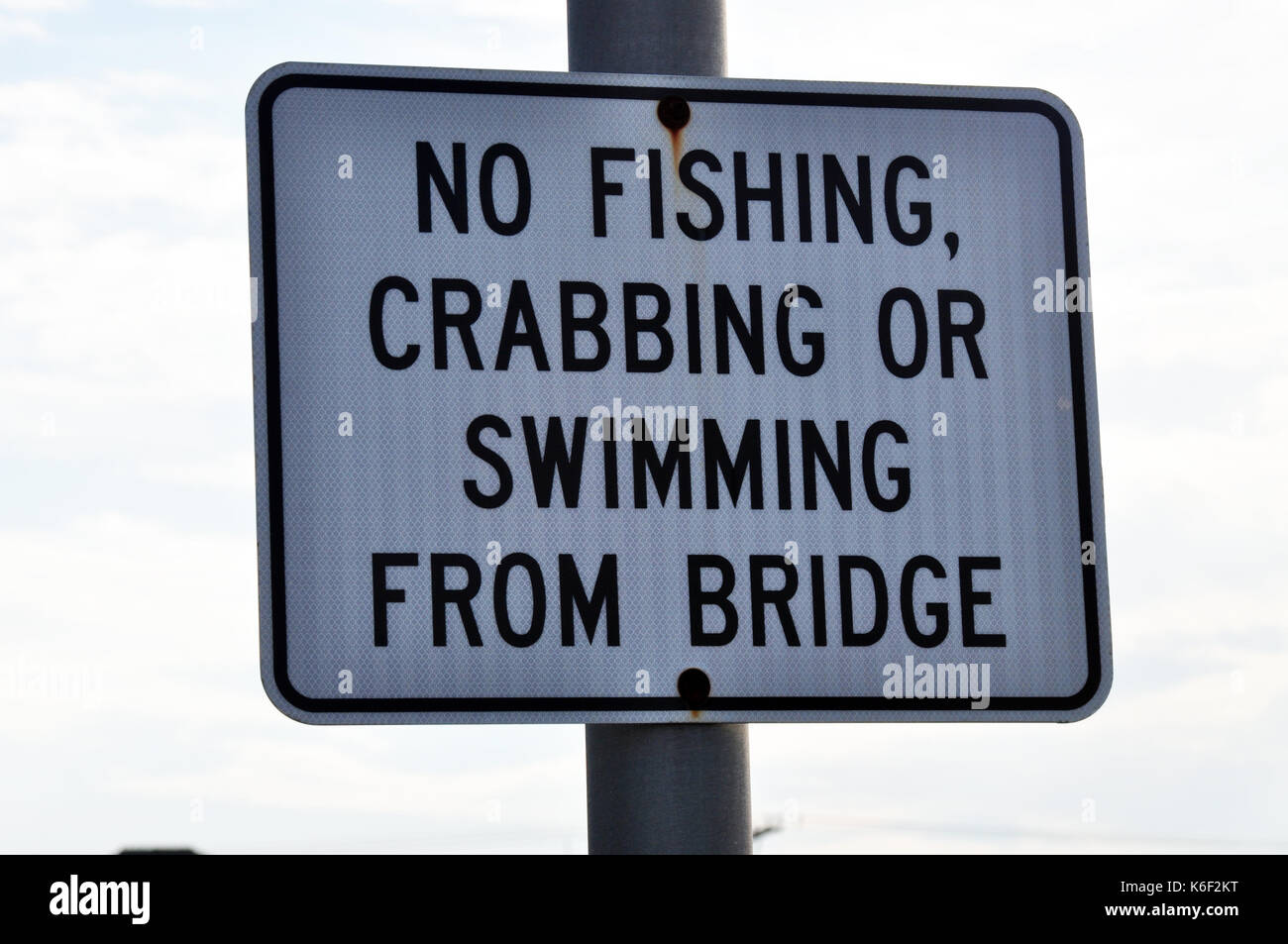 A Sign that reads 'No Fishing Crabbing or Swimming from Bridge'.  Black printing on a white background. Stock Photo