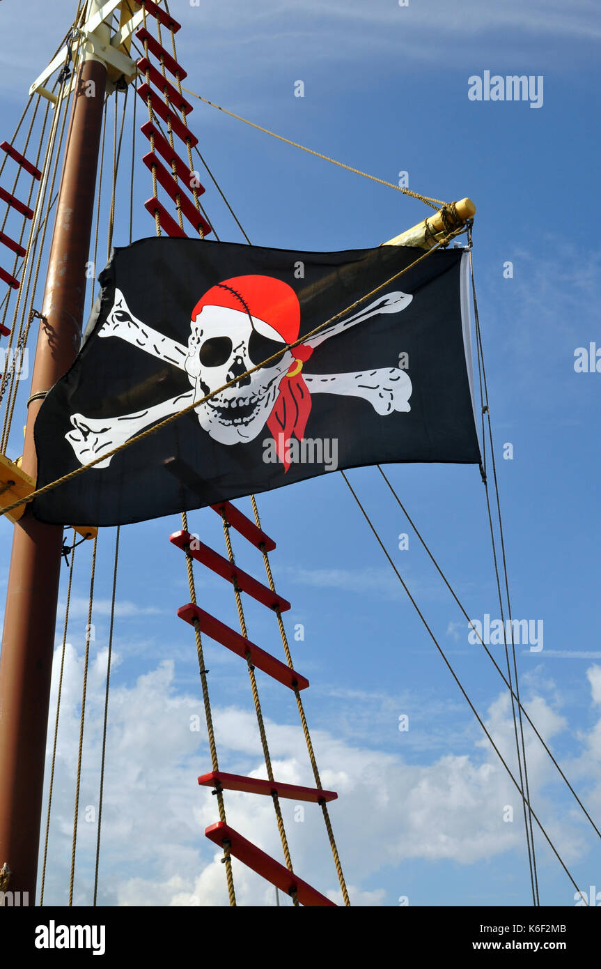 Black, White, and Red Pirate Flag flying on a ship against a blue sky. Stock Photo