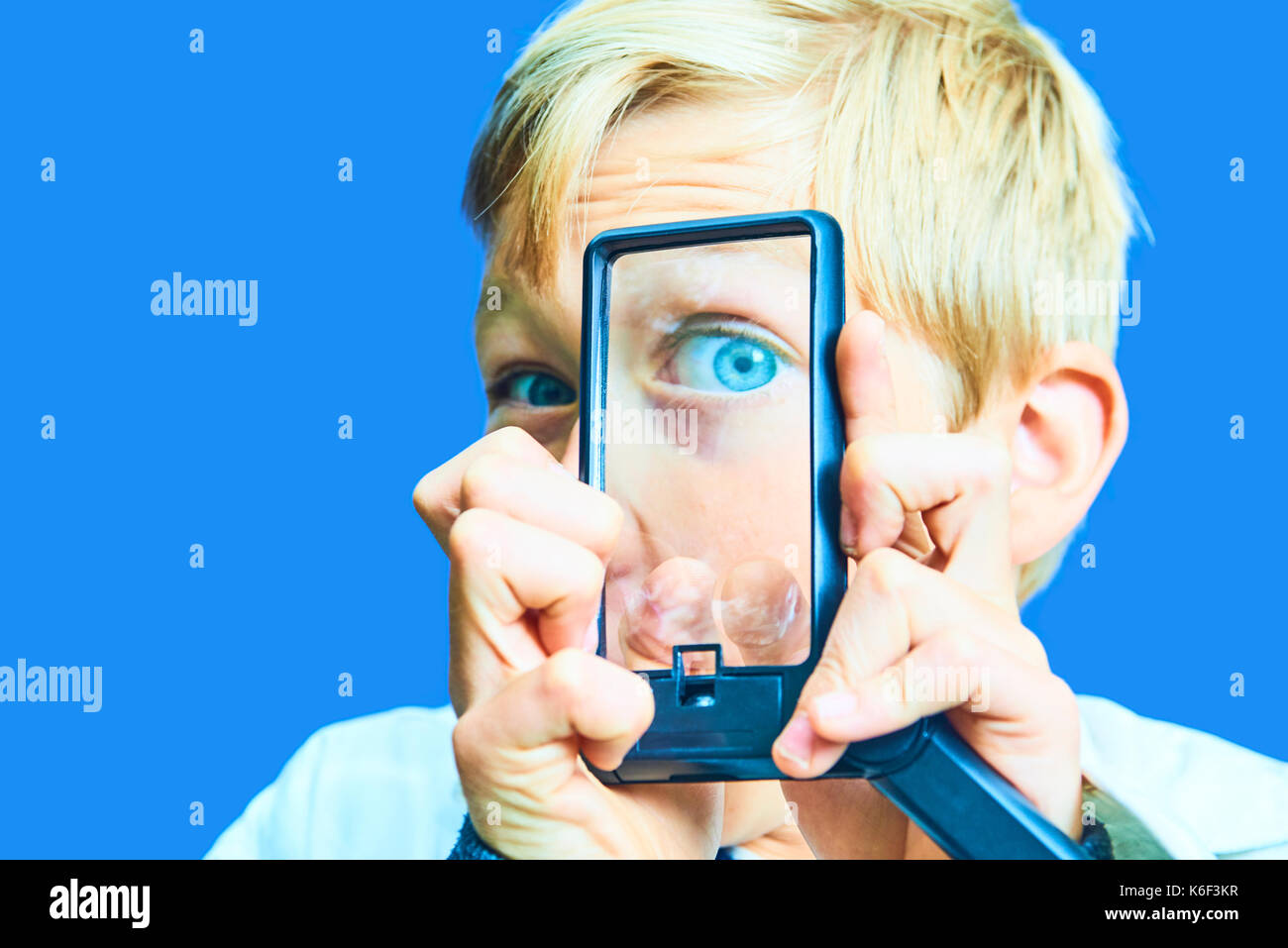 Portrait of Child Young Blond Boy using magnifying glass. Concept of crazy scientist. Isolated on blue keying background. Stock Photo