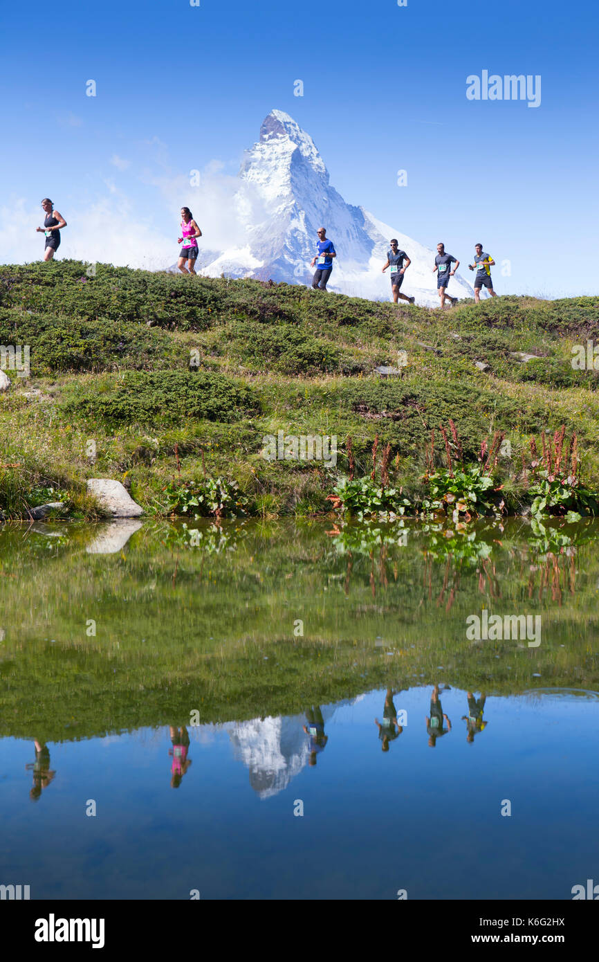 Trail runners in front of Matterhorn reflecting in lake, Zermatt, Valais, Switzerland Stock Photo