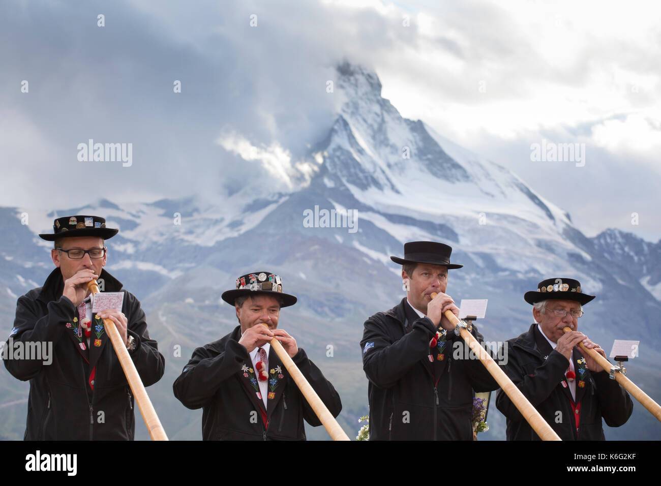 Four traditionally dressed locals playing alphorn against Matterhorn mountain, Zermatt, Valais, Switzerland Stock Photo