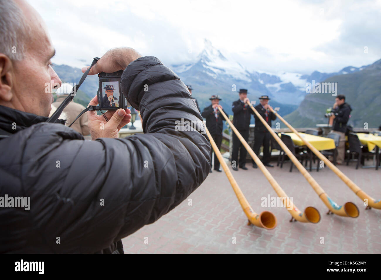 Tourist photographing men playing alpenhorns, Zermatt, Valais, Switzerland Stock Photo