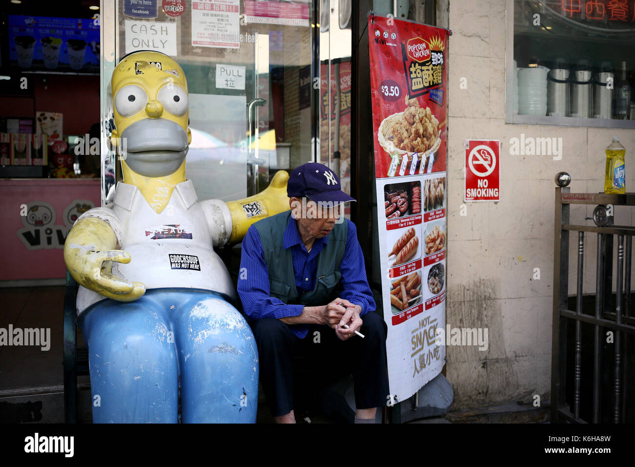 CHINATOWN, NEW YORK, USA - JUNE 2016 - An unidentified person sitting in a food shop stair next to a statue of homer simpson at Chinatown Stock Photo