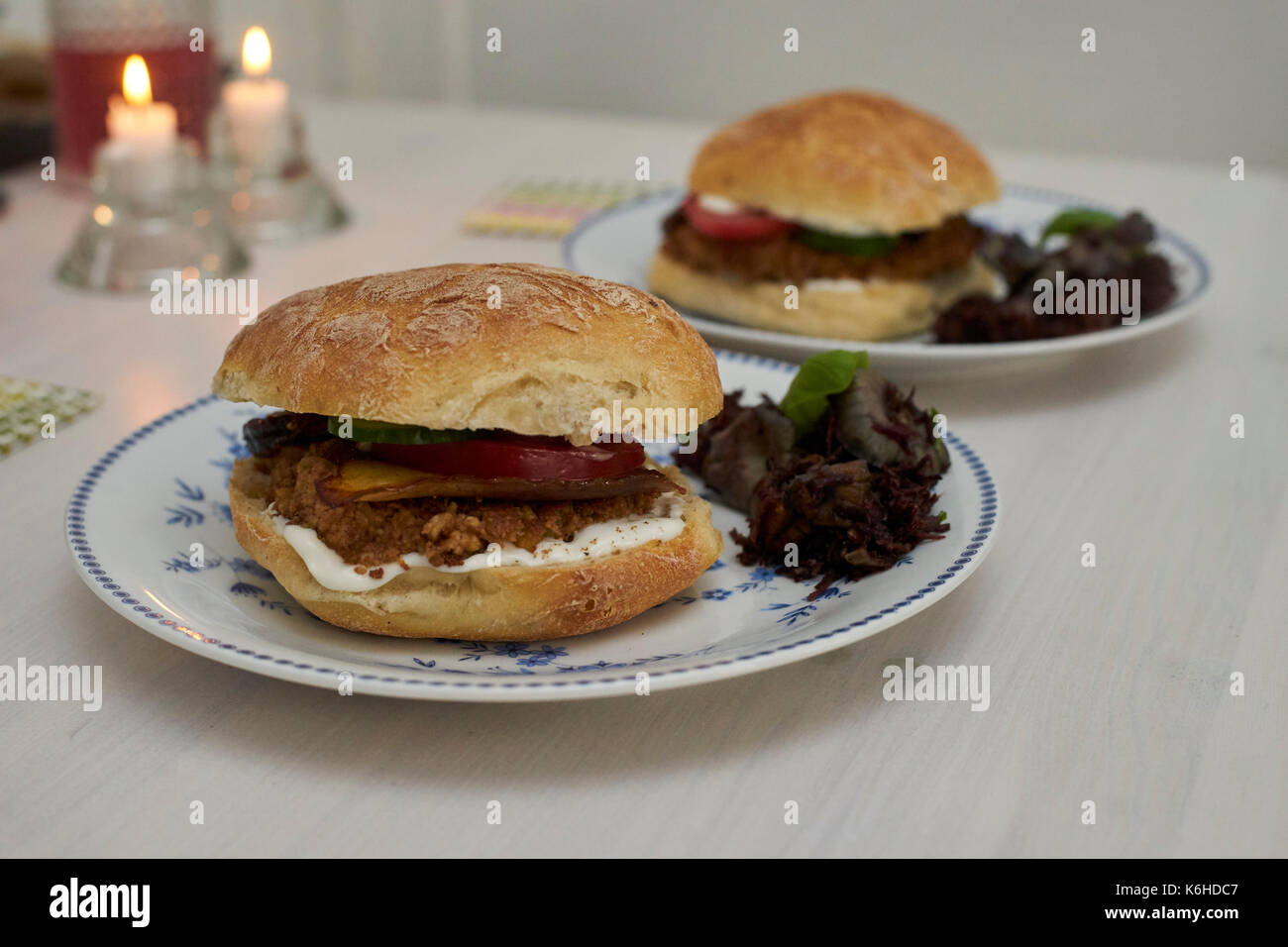Two vegan burgers on plates and two candles in the background Stock Photo