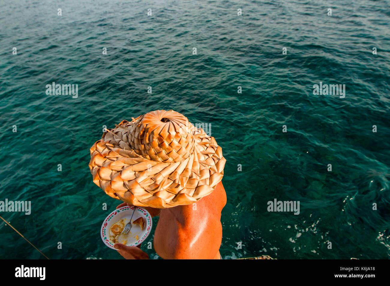 A man with a palm-frond hat eats breakfast on a sailboat near Utila Island, Honduras. Stock Photo