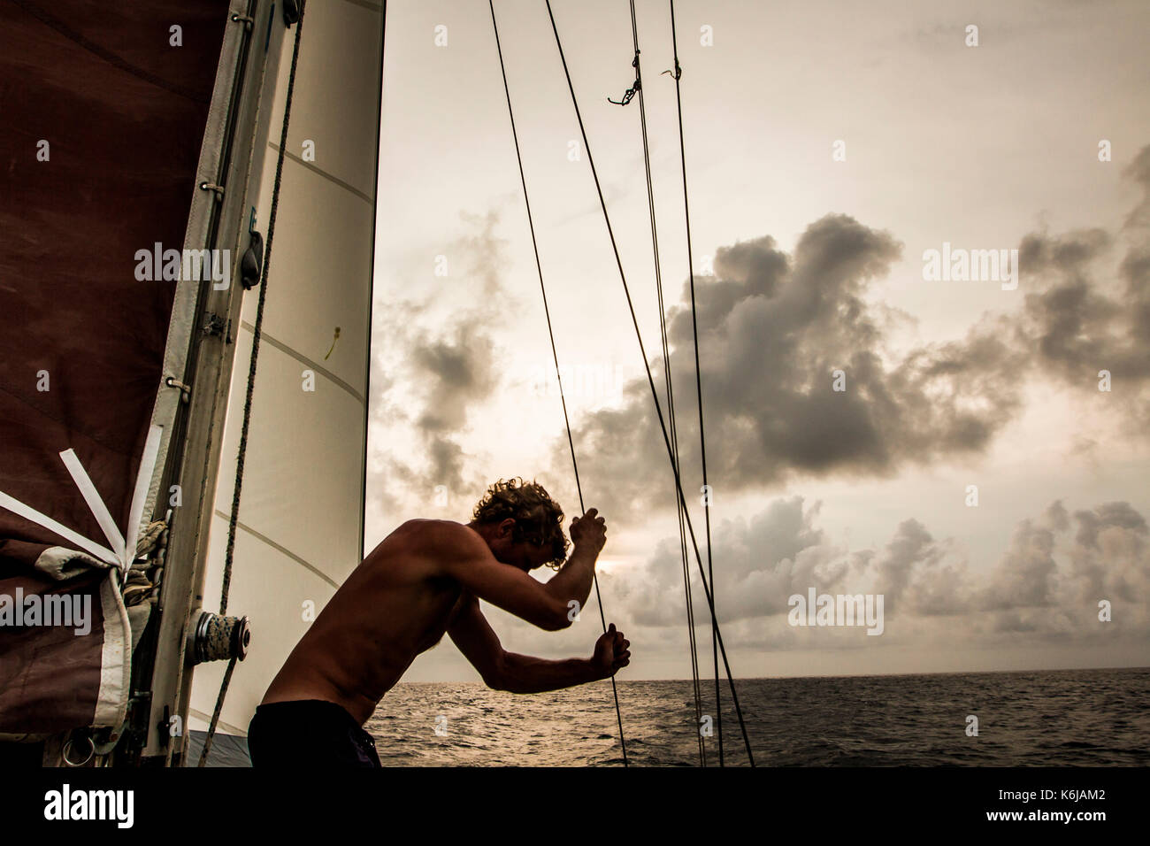 Shirtless man adjusting sails while sailing across Caribbean Sea, Honduras Stock Photo
