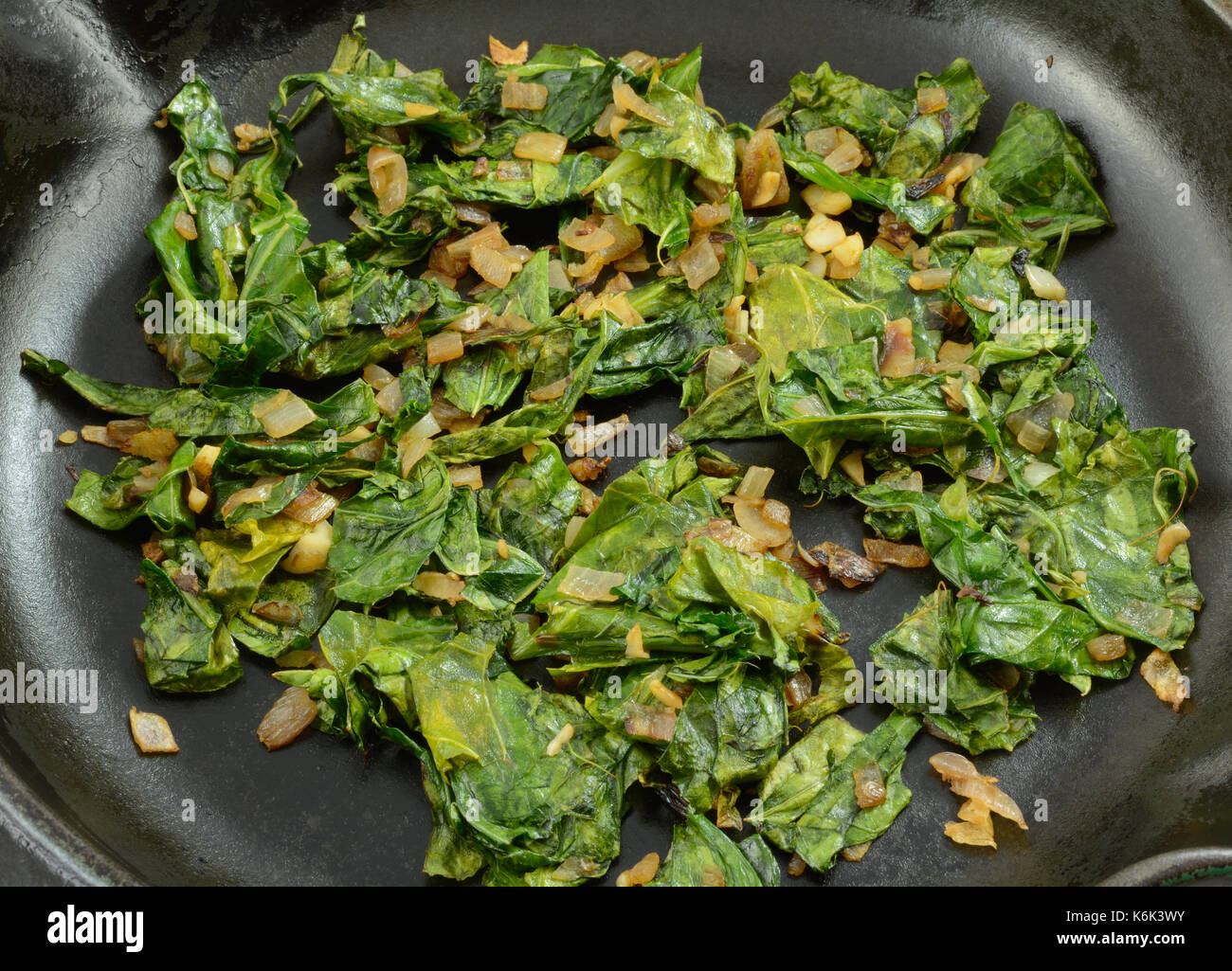 Close up of sauteed collard greens with chopped shallot in cast iron