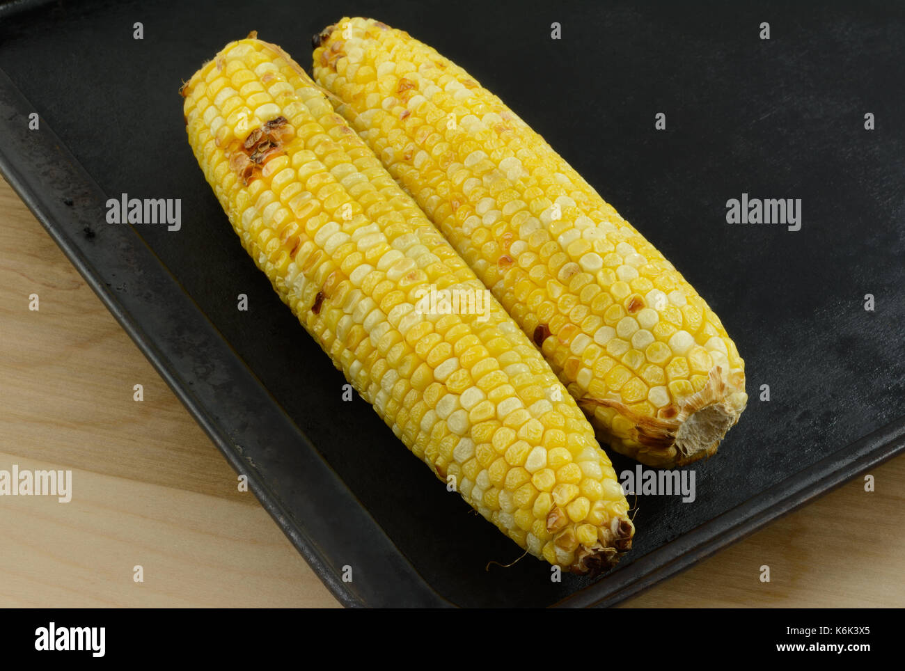 Two ears of blackened roasted corn on baking sheet Stock Photo