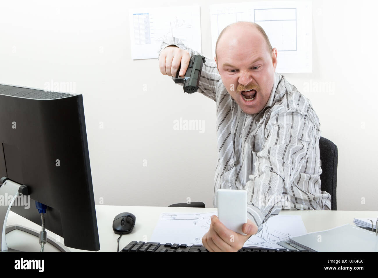 Businessman Aiming Gun On Mobile Phone At Desk Stock Photo