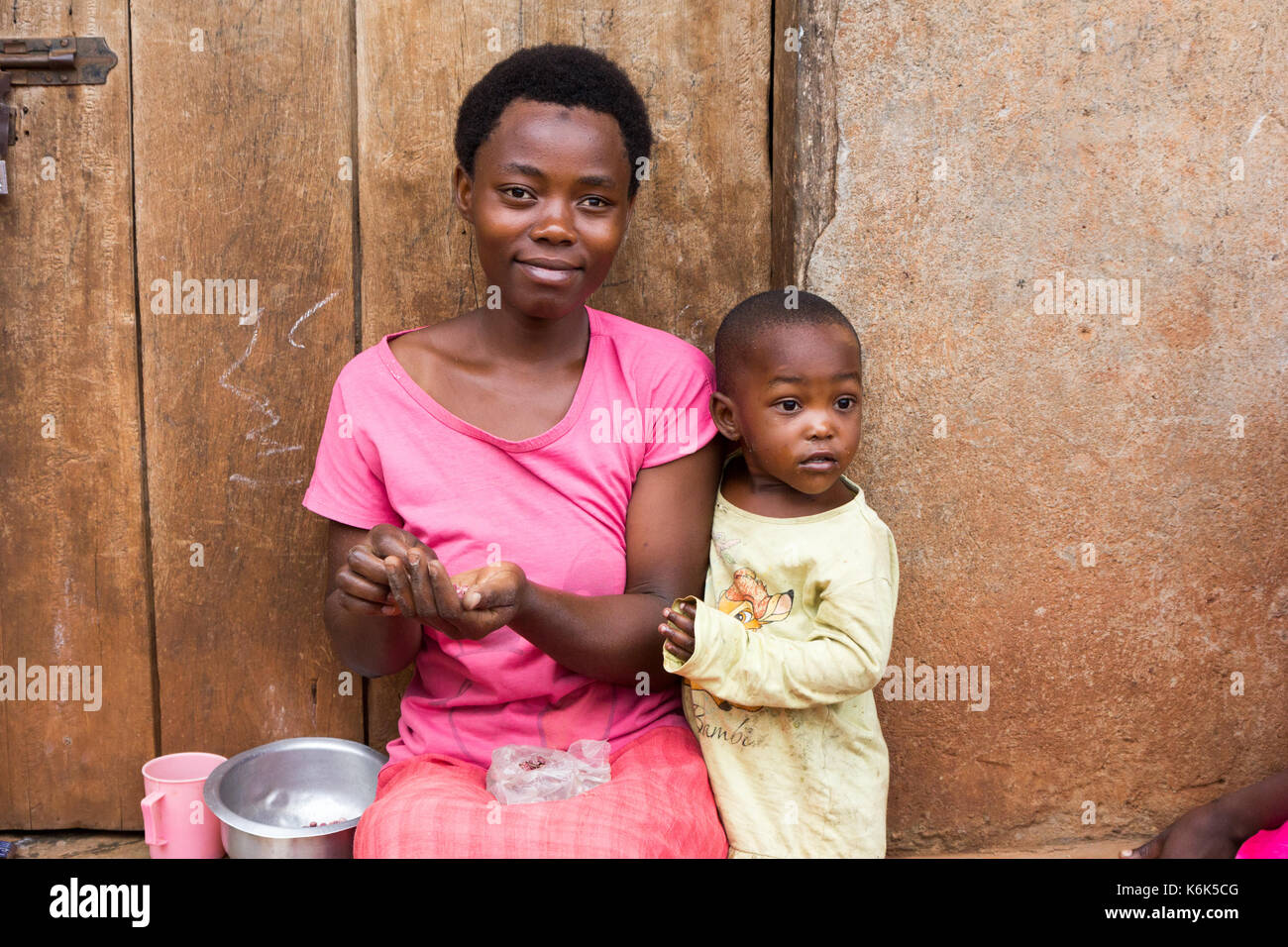Lugazi, Uganda. 09 June 2017. A laughing African mother with a little child boy. The woman is sitting on door threshold sorting grains. Stock Photo