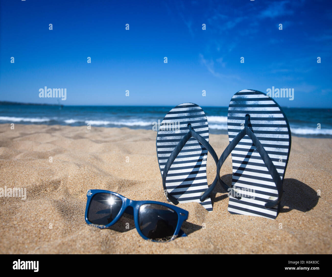 Blue sandal flip flop and sunglasses on the sand beach with blue sea ...