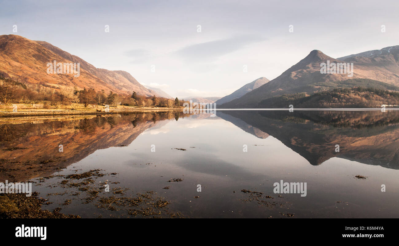 The distinctive shaped Pap of Glencoe mountain is reflected in the calm water of Loch Leven, a fjord-like inlet of the Atlantic Ocean, on a clear wint Stock Photo