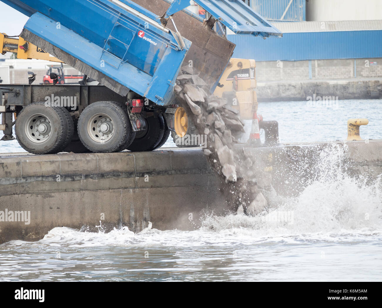 Tipper truck emptying rubble into sea as part of dock extension. Stock Photo