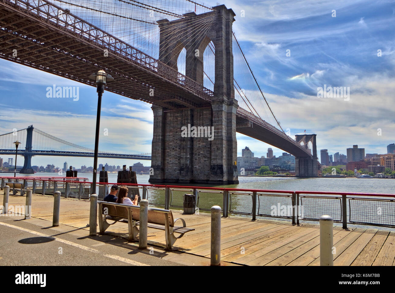 A couple sits on a park bench underneath the Brooklyn Bridge on the Manhattan side. Stock Photo