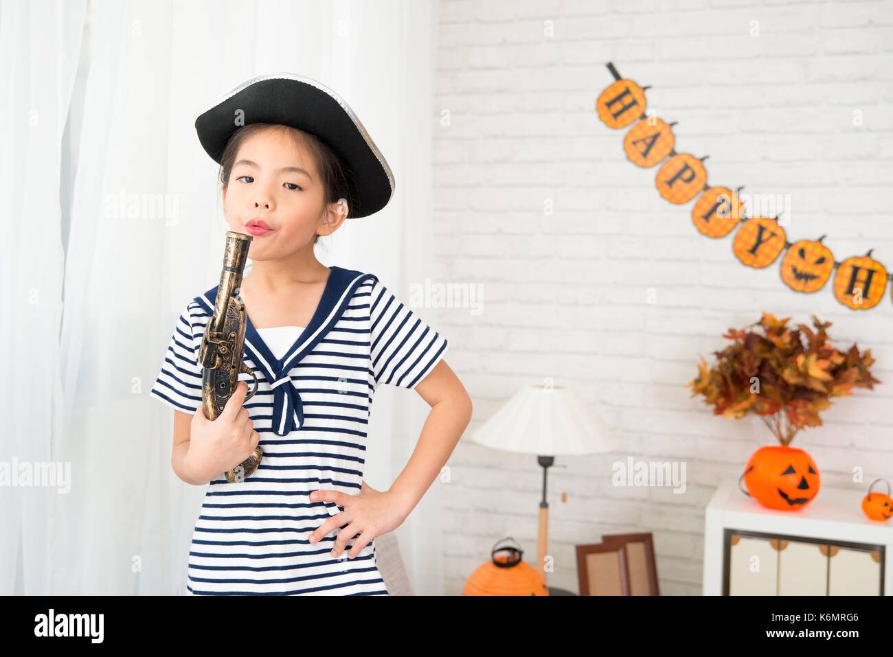 little pirate girl blowing toy gun after shooting have fun with her friends at Halloween party at home Stock Photo