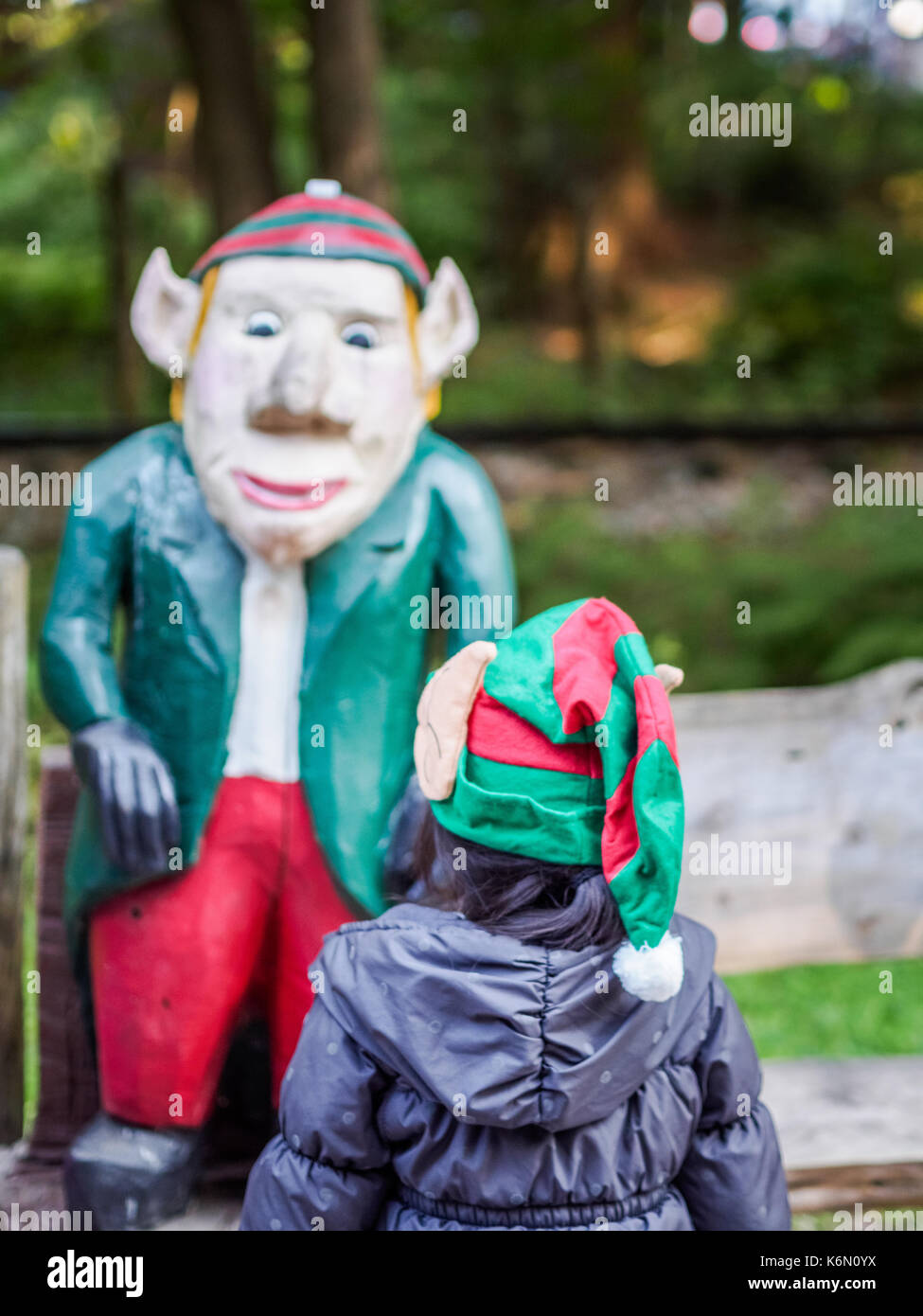 A child wearing Christmas hat viewing Christmas Elf Statue as seen in Santa Village, Bracebridge, Ontario, Canada Stock Photo