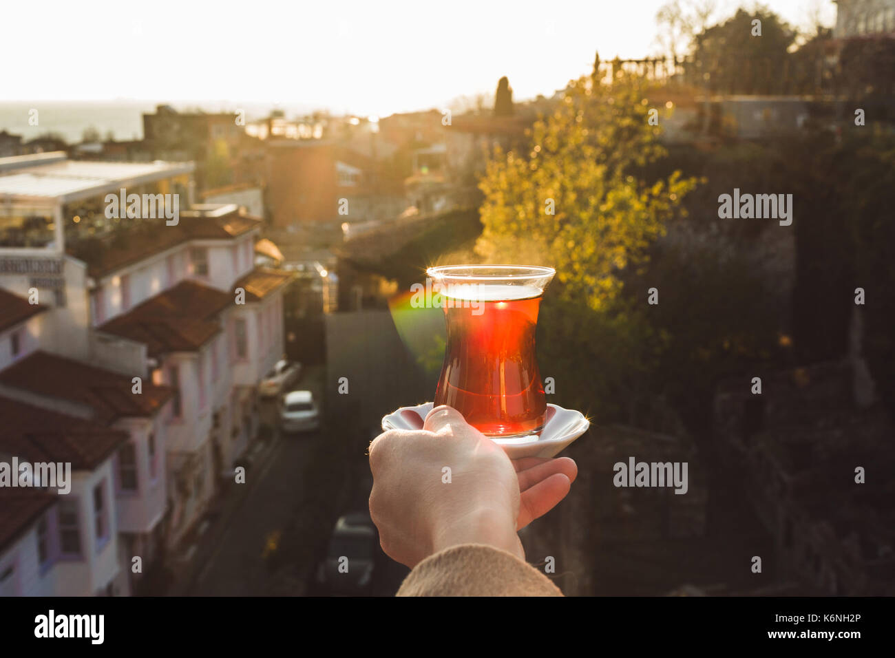 Hand holding a cup of traditional Turkish tea illuminated and transparent by the warm evening sunlight. Sunset teatime in Istanbul Stock Photo