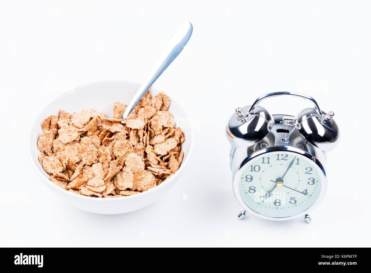 useful breakfast of cereal and alarm clock on white table closeup